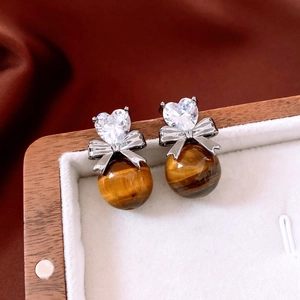 Macro detail of tiger eye bead earrings with silver bow and heart-shaped cubic zirconia