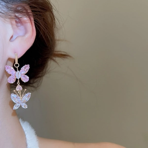Close-up of pink and clear crystal butterfly drop earrings worn by a model