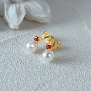 Macro view of gold stud earrings featuring round white pearls and sparkling red gemstones