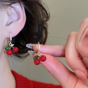 Close-up of cherry stud earrings with red beads, green leaf gems, and gold accents