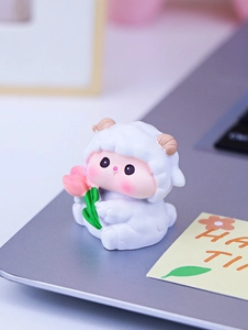 Mini resin white lamb figurine holding a pink tulip on a desk workspace