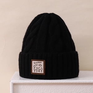Close-up of black cable-knit beanie featuring a Lucky cartoon bear patch detail