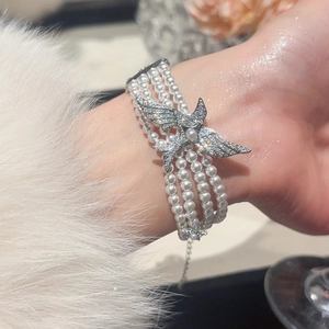 Détail d'un bracelet de perles multicouche avec un charm oiseau en zircone et fermoir