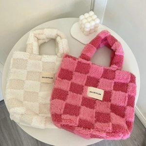 Close-up of plush checkerboard bucket bags in cream and pink on a white table