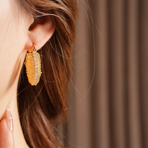Close-up of gold-plated geometric hoop earrings with sparkling cubic zirconia on a model