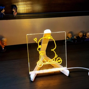 Close-up of lit acrylic glow board with cartoon drawing and USB power cable on wood base