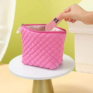 Pink quilted cosmetic bag being filled with a small organizer box on a minimalist display
