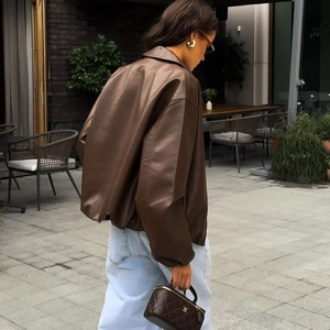 Brown faux leather jacket with high collar and loose fit shown in a street style outdoor view