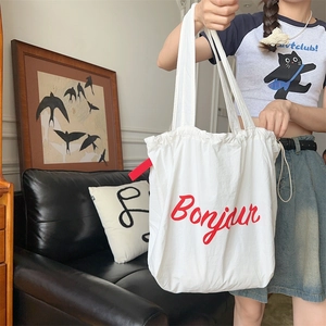 Detail of white canvas tote bag with red Bonjour lettering and drawstring closure