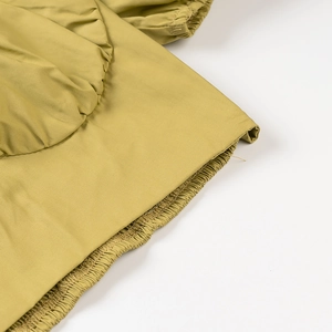 Detail of ginger yellow top featuring elastic ruffled edges and double stitched seams