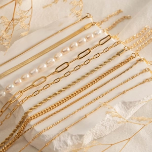 Detailed flat lay of assorted gold plated stainless steel layered chains and pearl necklaces