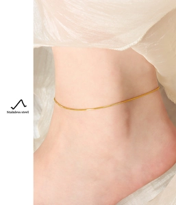 Detailed view of an 18K gold plated snake chain anklet worn on the ankle with soft lighting