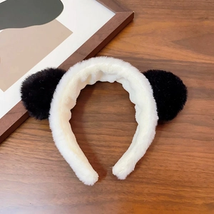 Close-up of a white plush headband with black panda ears on a dark wooden surface