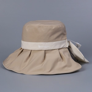 Macro detail of beige wide-brim UV sun hat featuring decorative strap and brand logo