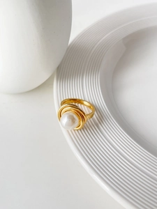 Détail macro d'une bague perle enveloppée de fil doré sur une assiette en céramique