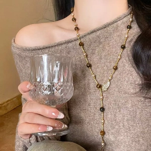 Detail of tiger eye stone necklace with wing pendant worn with elegant brown sweater