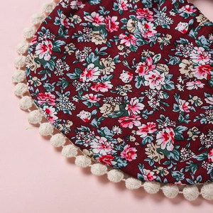Détail d'un bavoir floral rouge avec bordure à pompons blancs et texture en coton doux