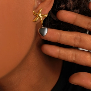 Detailed close-up of two-tone starfish and heart drop earrings worn on model's ear
