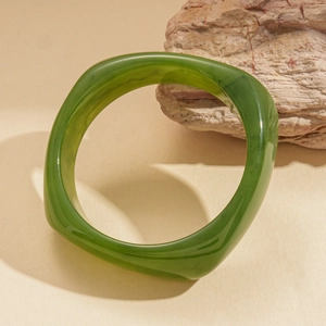 Deep green resin geometric bangle with marble texture displayed on a decorative stone