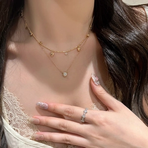 Dettaglio della collana dorata a due strati con cuore e anello a fiore di diamanti