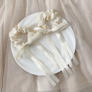 Elegant set of two cream satin bow hair scrunchies displayed on a white ceramic plate