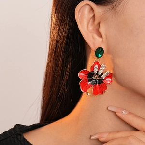Gros plan de boucles d'oreilles fleur en émail rouge avec strass et pierres vertes