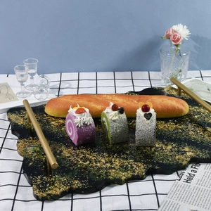 Irregular green resin tray with gold foil and metal handles holding bread and cakes