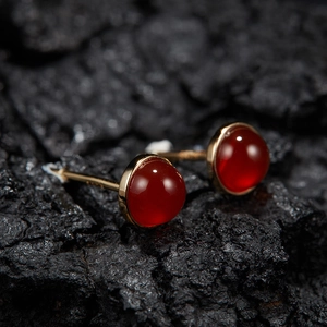 Macro shot of red round gemstone earrings in gold setting on black charcoal background