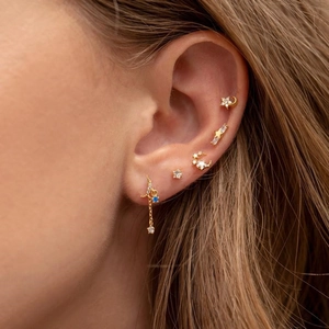 Detailed macro view of a gold-tone star and moon earring set with blue zircon on female model