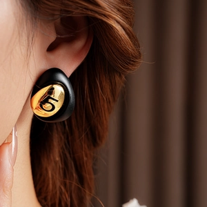 Detail showing a black enamel teardrop earring with gold-plated number five engraving