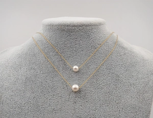 Close-up of a layered gold necklace featuring two white pearl pendants on a grey model