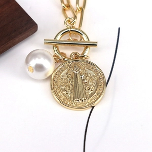 Close-up of gold coin medallion and white pearl pendant on a geometric toggle necklace