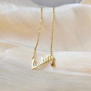 Close-up of a gold custom Lolita name necklace with a small red birthstone on satin