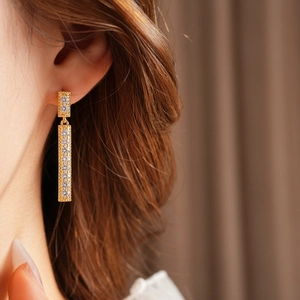 Gros plan de boucles d'oreilles dorées à pompons carrés avec zircons brillants sur un modèle