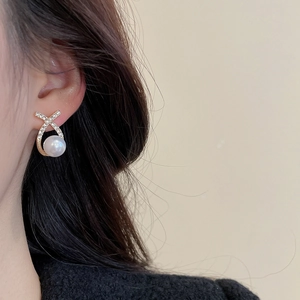 Detail showing elegant X-shaped gold earrings with diamonds and white round pearl on ear
