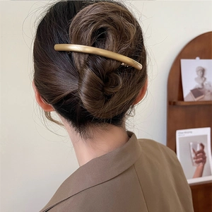 Minimalist matte gold curved metal hair claw clip worn on a bun hairstyle for women