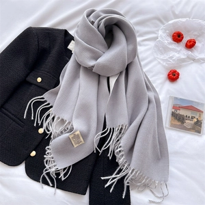 Flat lay of grey cashmere-like scarf with fringe detail and a woven label on white linen