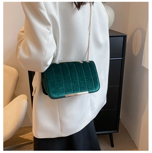Dark green velvet chain bag worn over a white suit jacket for a stylish casual look