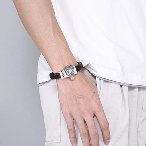 Detail of woven black leather bracelet featuring a silver wolf head clasp on a male wrist