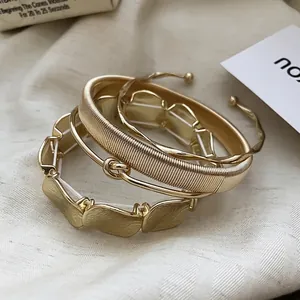 Three-piece set of textured golden metal bangles including spring and knot designs