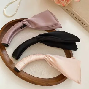 Trois pinces à cheveux élégantes en satin rose, noir et beige sur un plateau en bois