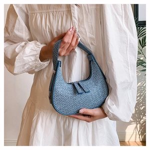 Detailed blue woven texture on crescent shoulder bag held by a model in a white dress