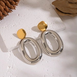 Close-up of two-tone gold and silver oval hoop earrings on a textured stone surface
