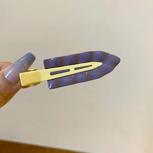 Detail showing wavy purple resin panel and yellow duckbill clip texture on a hair clip