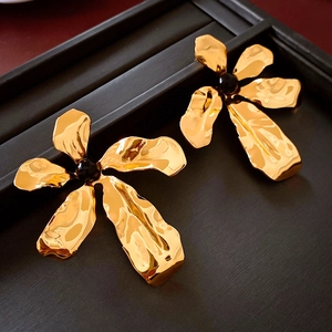Macro detail of gold flower earrings with hammered texture and black gemstone centers