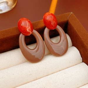 Close-up of vintage oval cutout earrings with red resin tops on a beige jewelry cushion