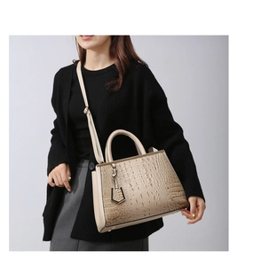 Detail shot of the crocodile embossed texture and metal charm on a beige shoulder bag