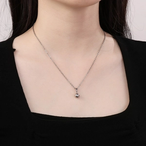 Close-up of a minimalist silver ball pendant on a fine metal chain worn by a model