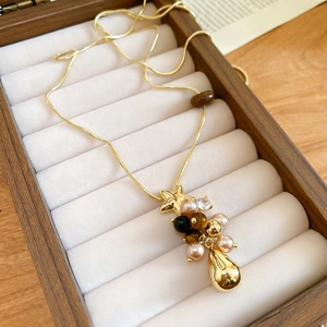 Détail macro d'un collier doré orné de perles, d'une étoile et d'un pendentif goutte d'eau