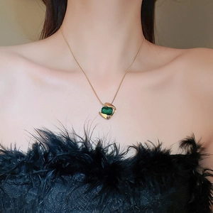 Close-up of a gold snake chain necklace with a green square gemstone on a model's neck